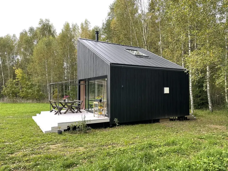 Black timber cabin with a terrace among birch trees